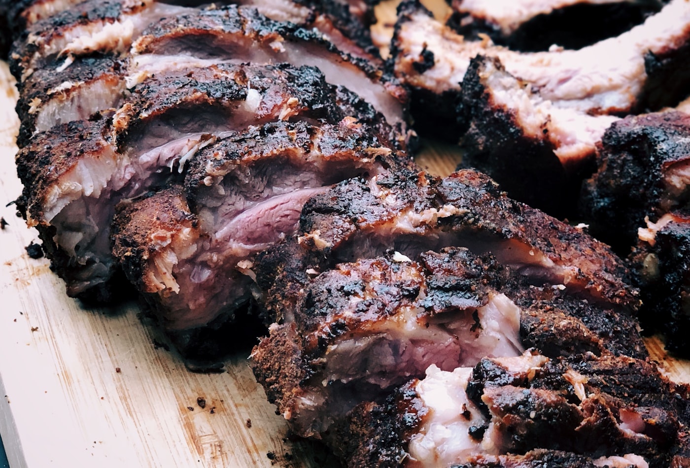 Slow-smoked ribs with a dark bark, sliced on a wooden board