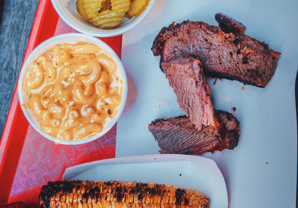 Smoked brisket with a tub of macaroni cheese, pickles and charred corn on a tray